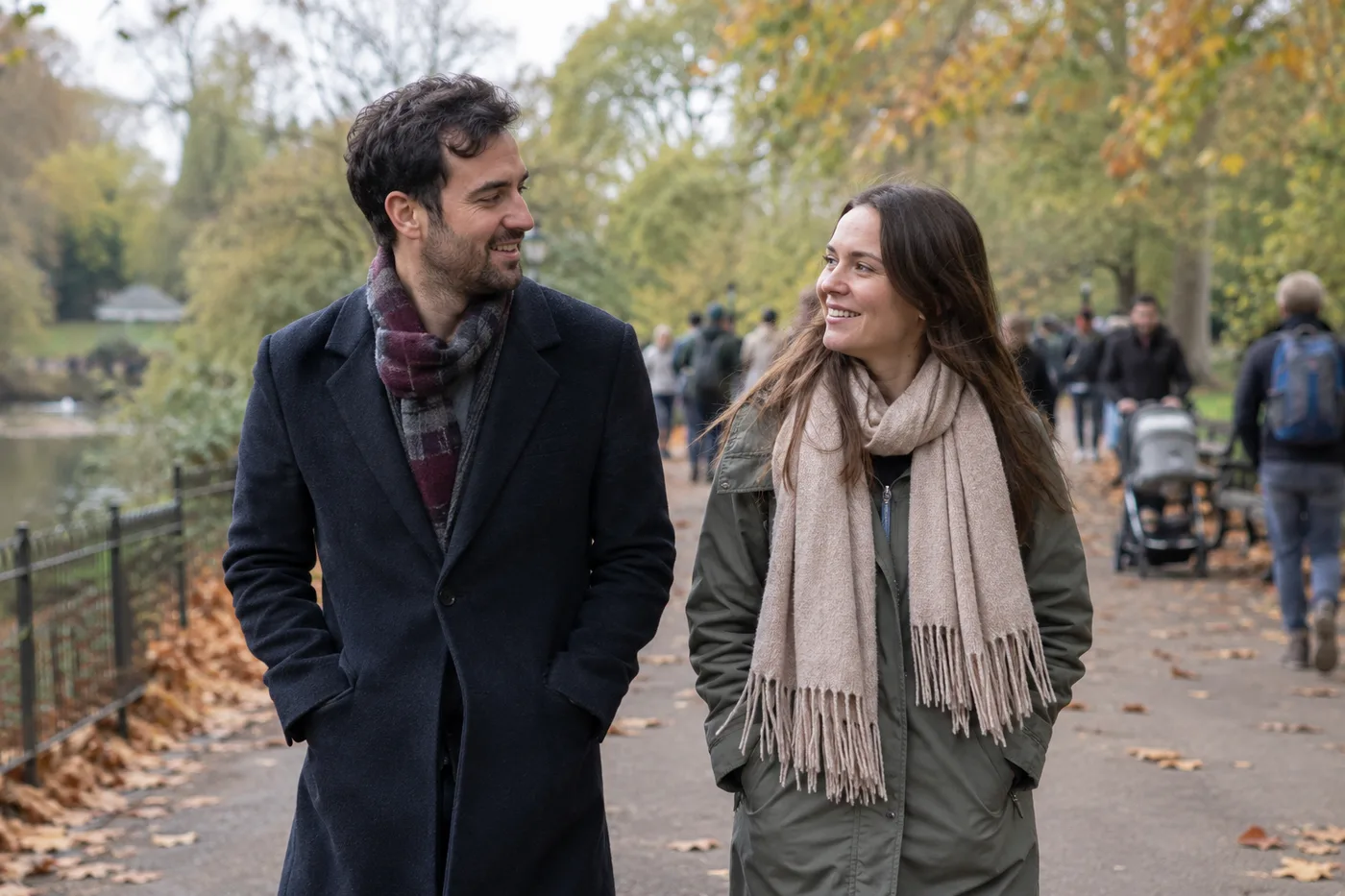 Two adults in coats walking together along a busy autumn park path